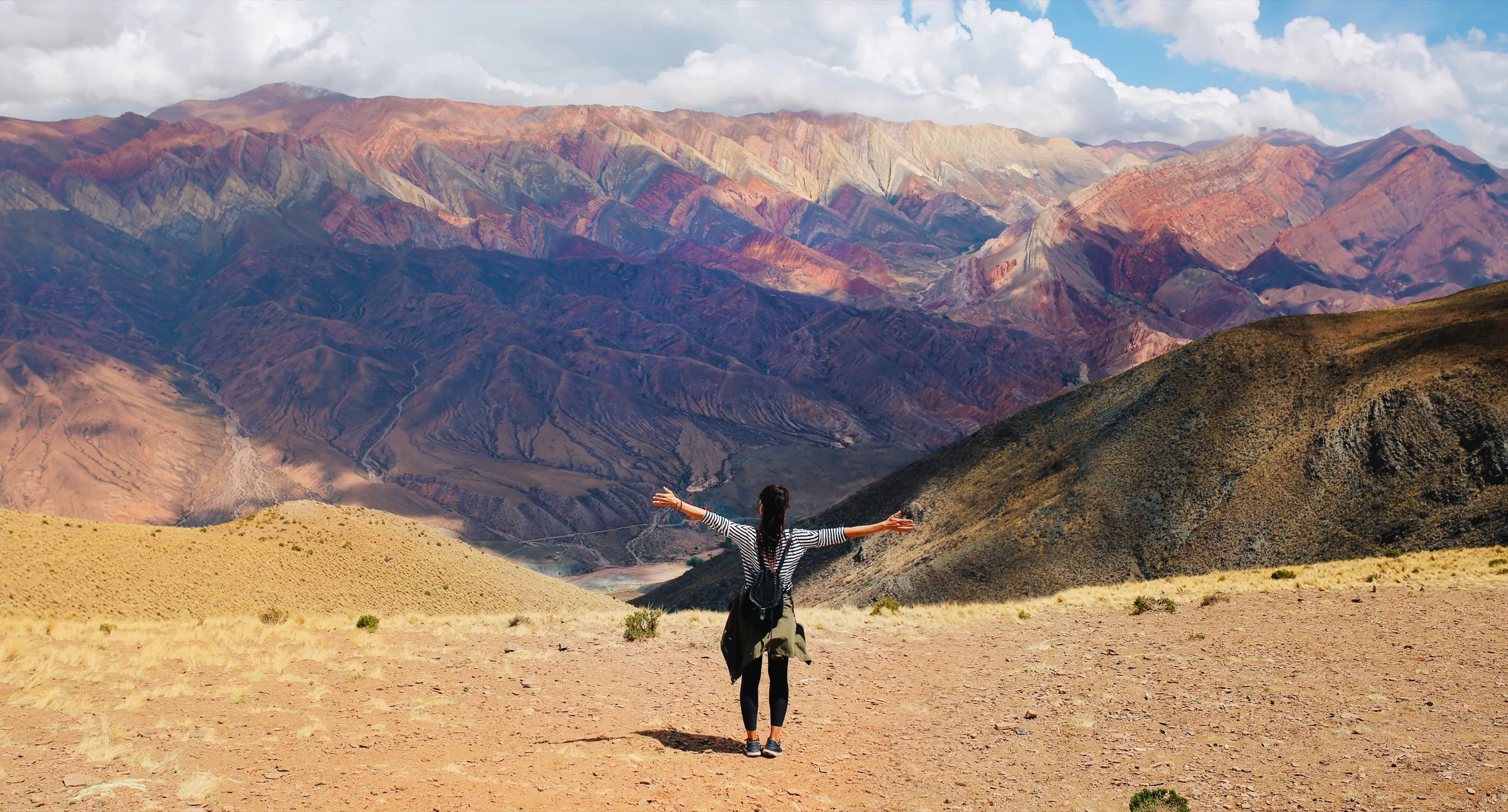 A traveler with arms outstretched before the rainbow-striped mountains of Hornocal, Argentina