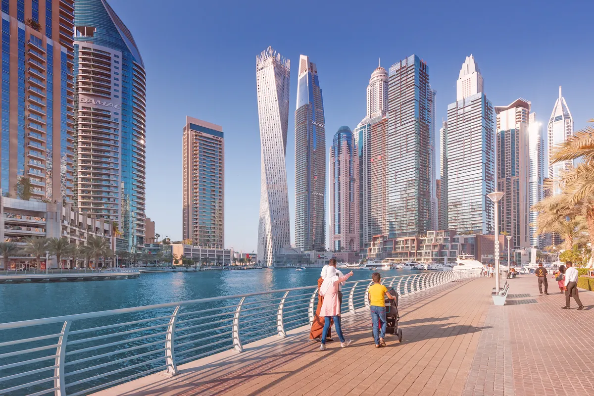 A family walking along the Dubai Marina promenade beneath its skyscrapers