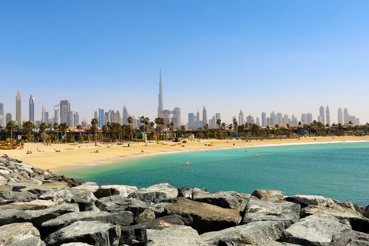 Dubai's skyline and the Burj Khalifa beyond a turquoise bay and a sandy beach