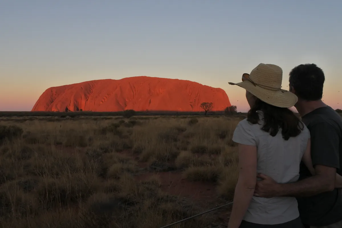 A couple watching Uluru glow red at sunset across the desert